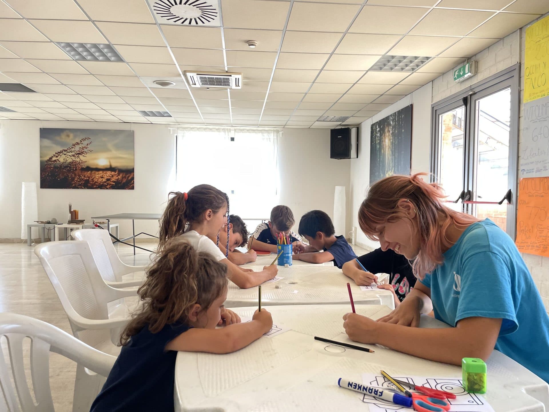 Bambini che disegnano al tavolo con un'animatrice, nelle sale climatizzate di Wellness Town